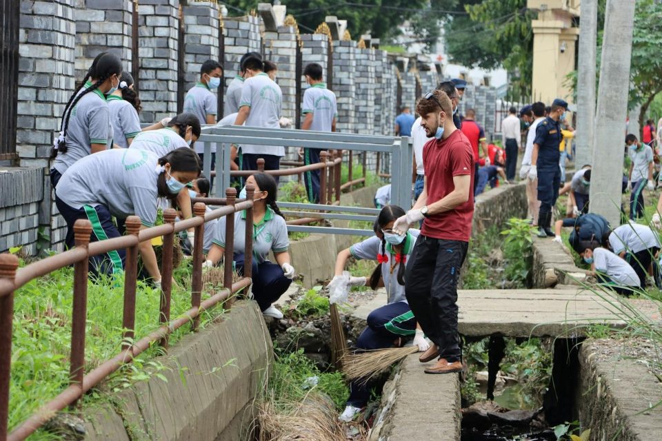 Group of volunteers in masks participating in outdoor canal cleanup effort.